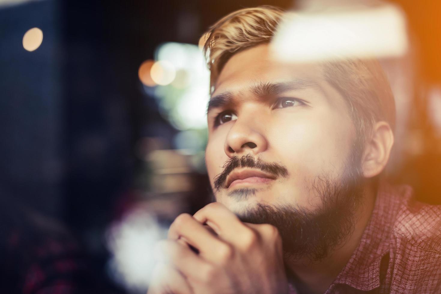 nachdenklicher junger Hipster-Mann, der in einem Coffeeshop-Denken sitzt foto