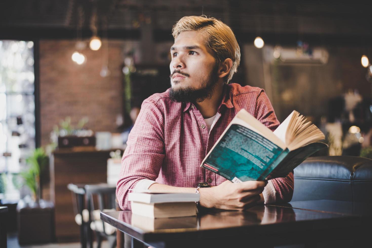 junger bärtiger Hipster, der ein Buch in einem Café liest foto