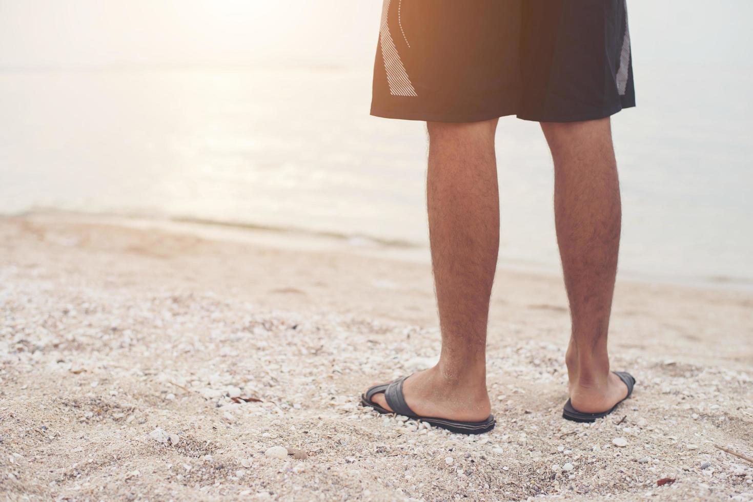 Beine des jungen Mannes in Sandalen am Strand foto