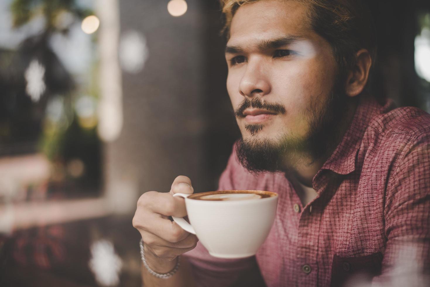 junger Mann, der in einem Café sitzt und einen Kaffee trinkt foto