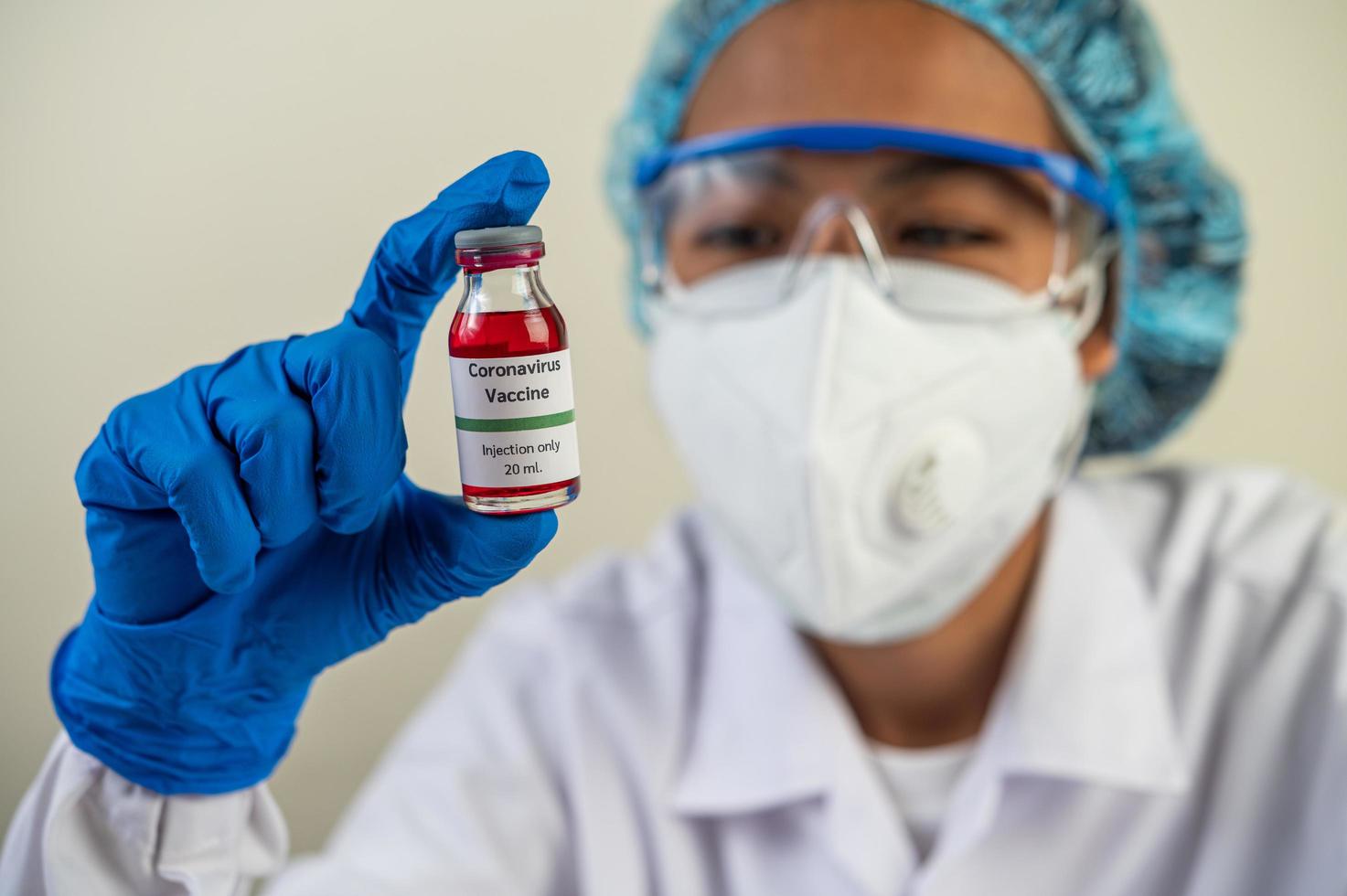 Ein Wissenschaftler, der Maske und Handschuhe trägt, trägt Fläschchen mit Impfstoffen zum Schutz vor Covid-19 foto