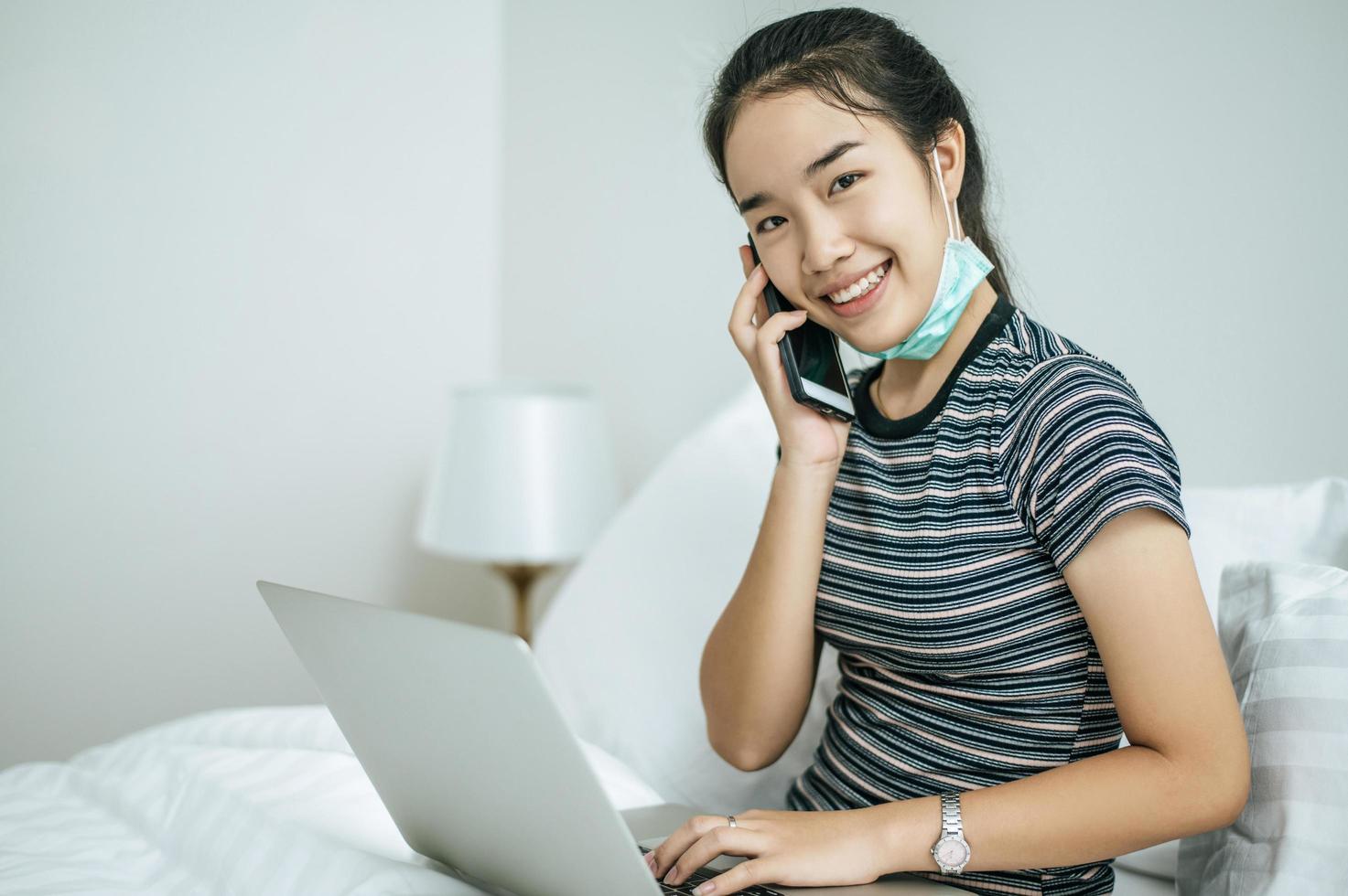 Frau spielt auf ihrem Laptop und spricht am Telefon foto