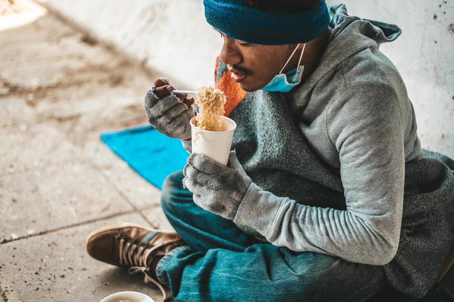 Obdachloser in Stoff gewickelt und Nudeln essen foto