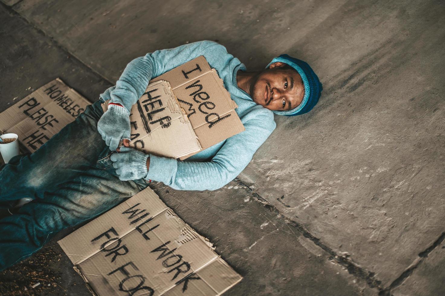 Bettler unter der Brücke mit einer Tasse Instantnudeln und einem Hilfeschild foto