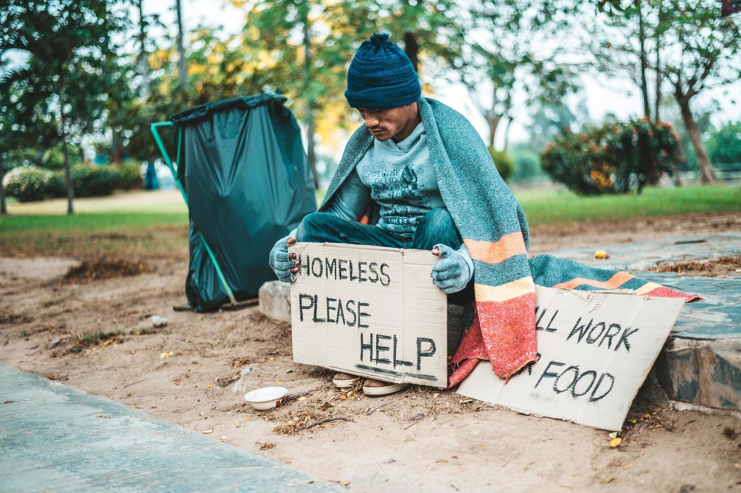 Ein Mann, der mit Obdachlosen sitzt, hilft bitte foto
