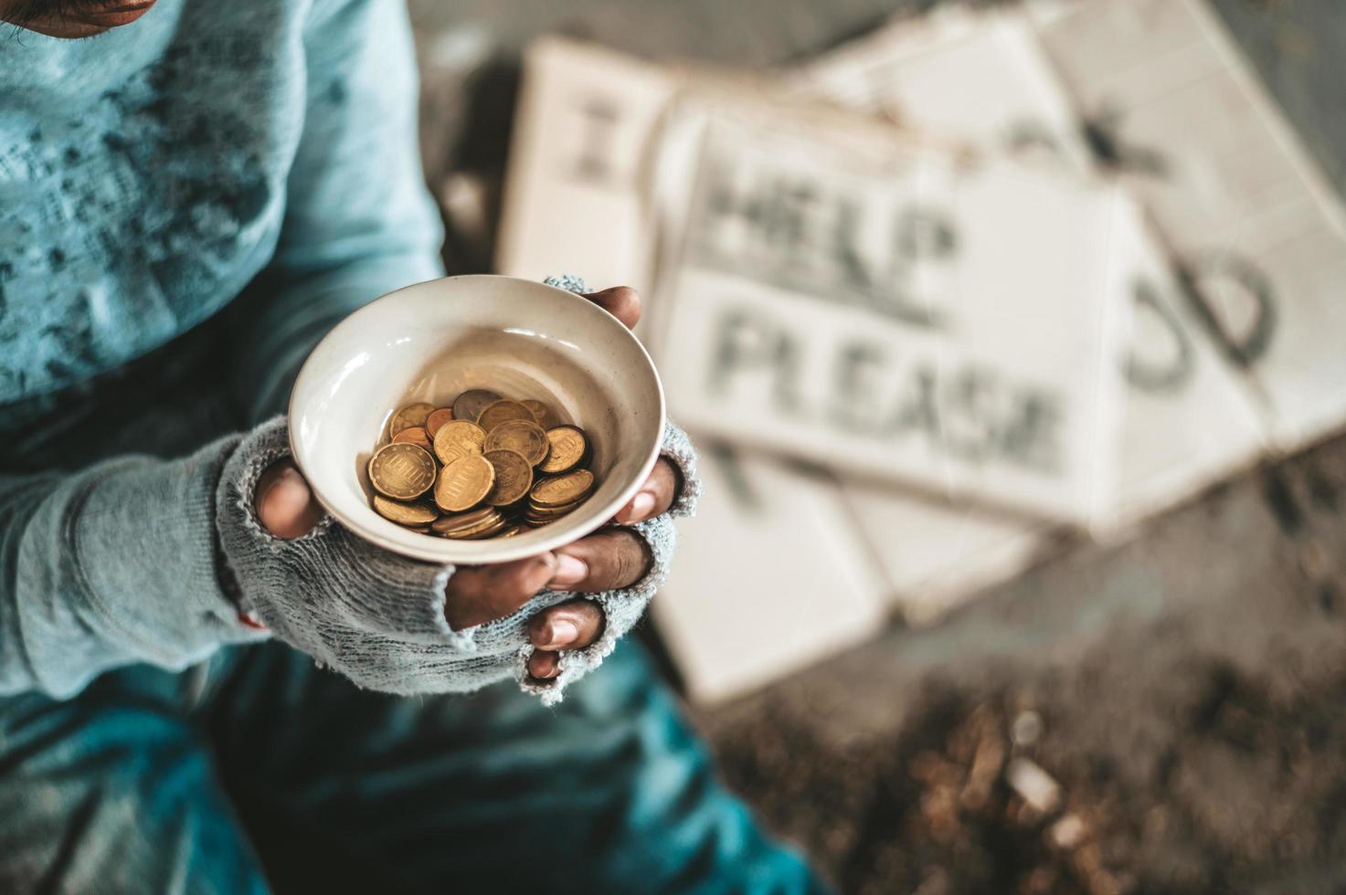 Bettler sitzt unter einer Brücke mit einer Tasse Geld foto