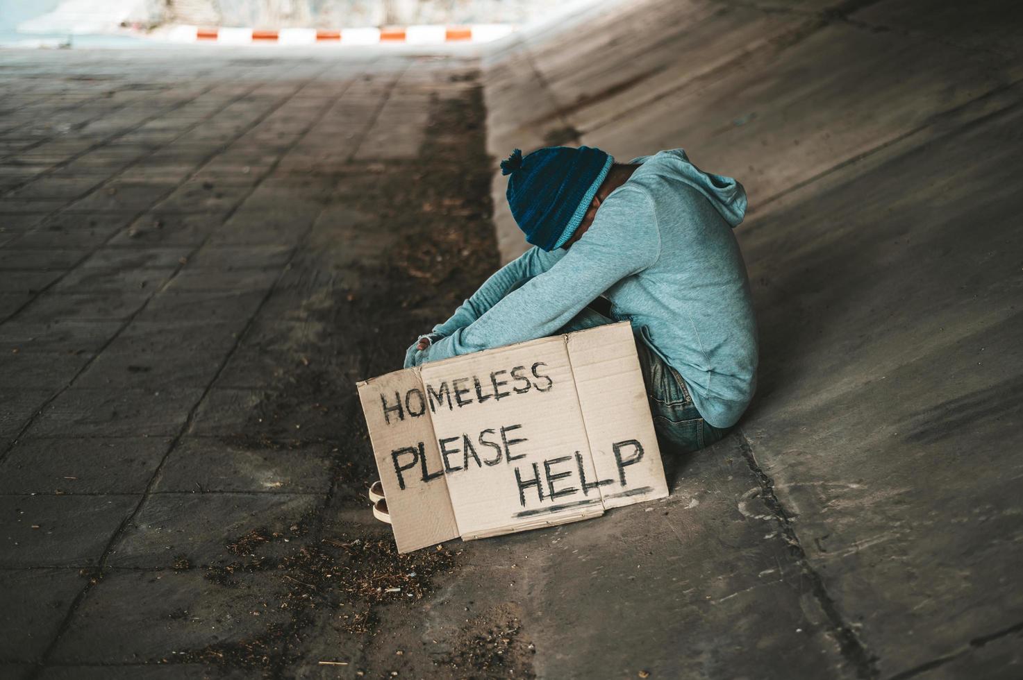Bettler sitzt unter der Brücke mit einer obdachlosen Nachricht foto
