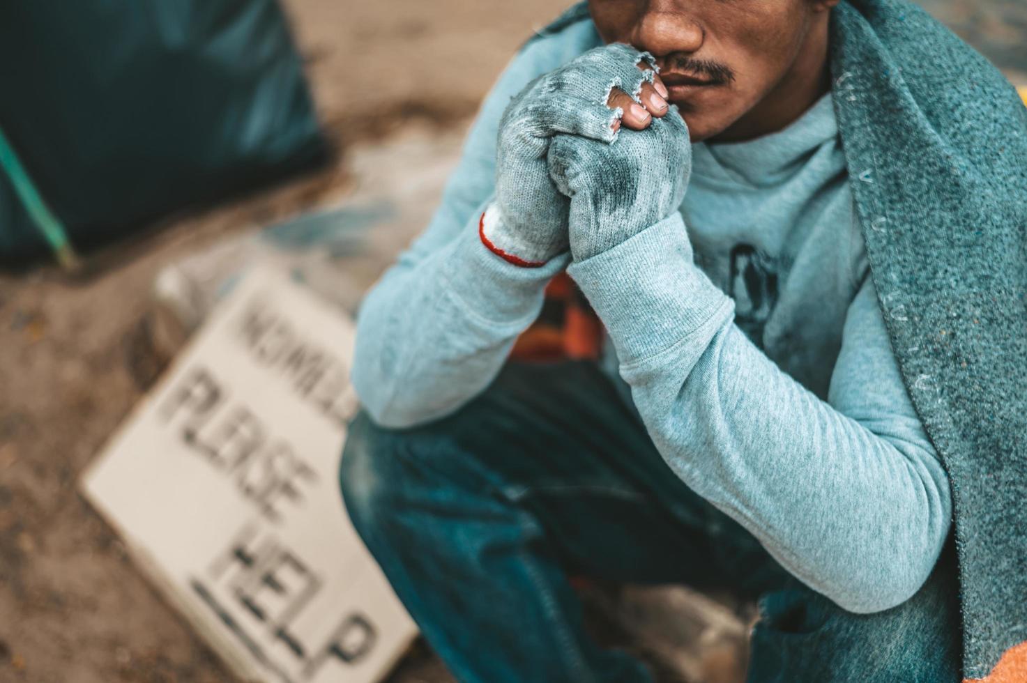 Ein Bettler sitzt draußen mit bitte helfen Zeichen foto