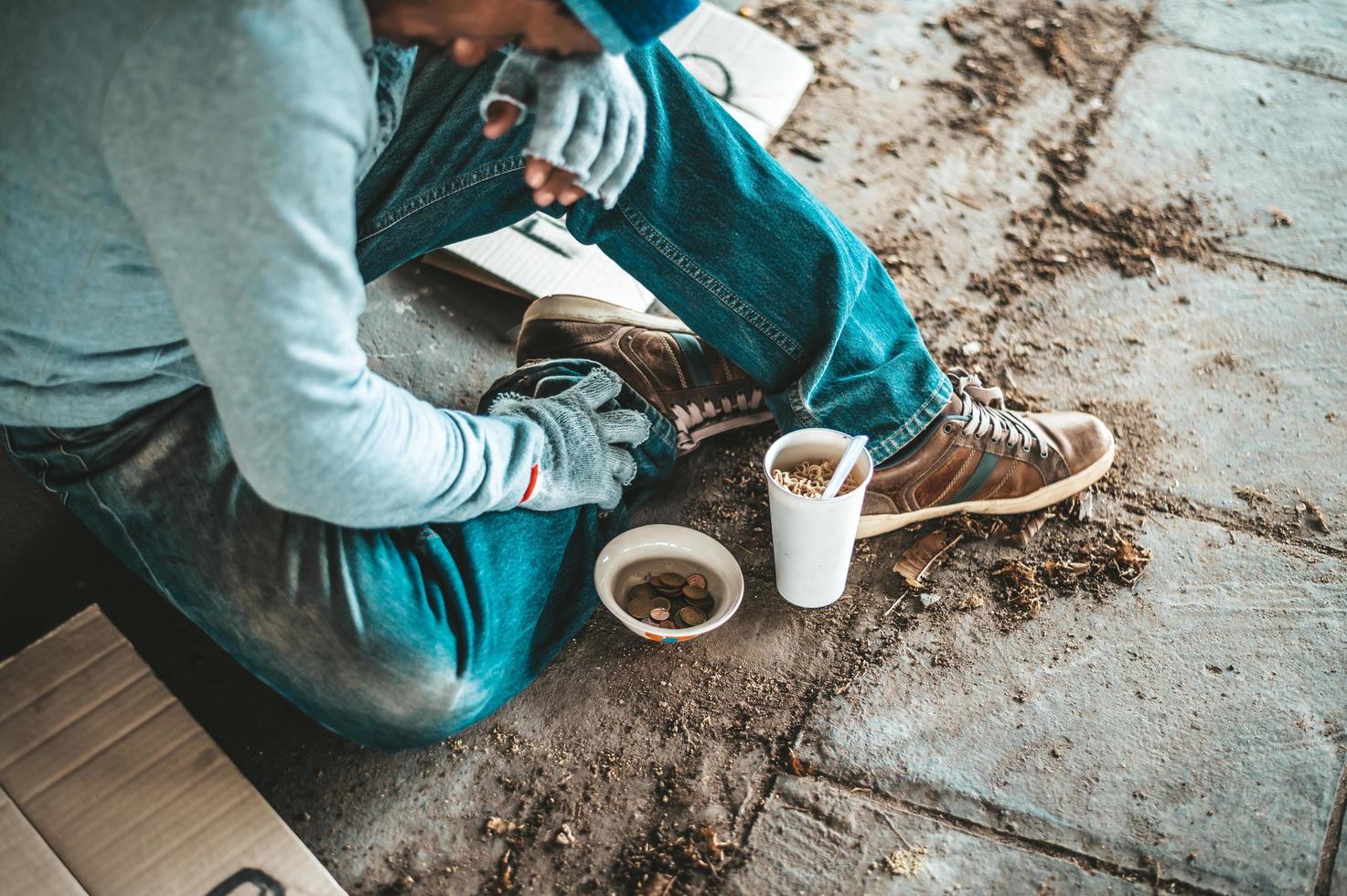 Betteln unter der Brücke mit einer Tasse mit Münzen und Instantnudeln foto