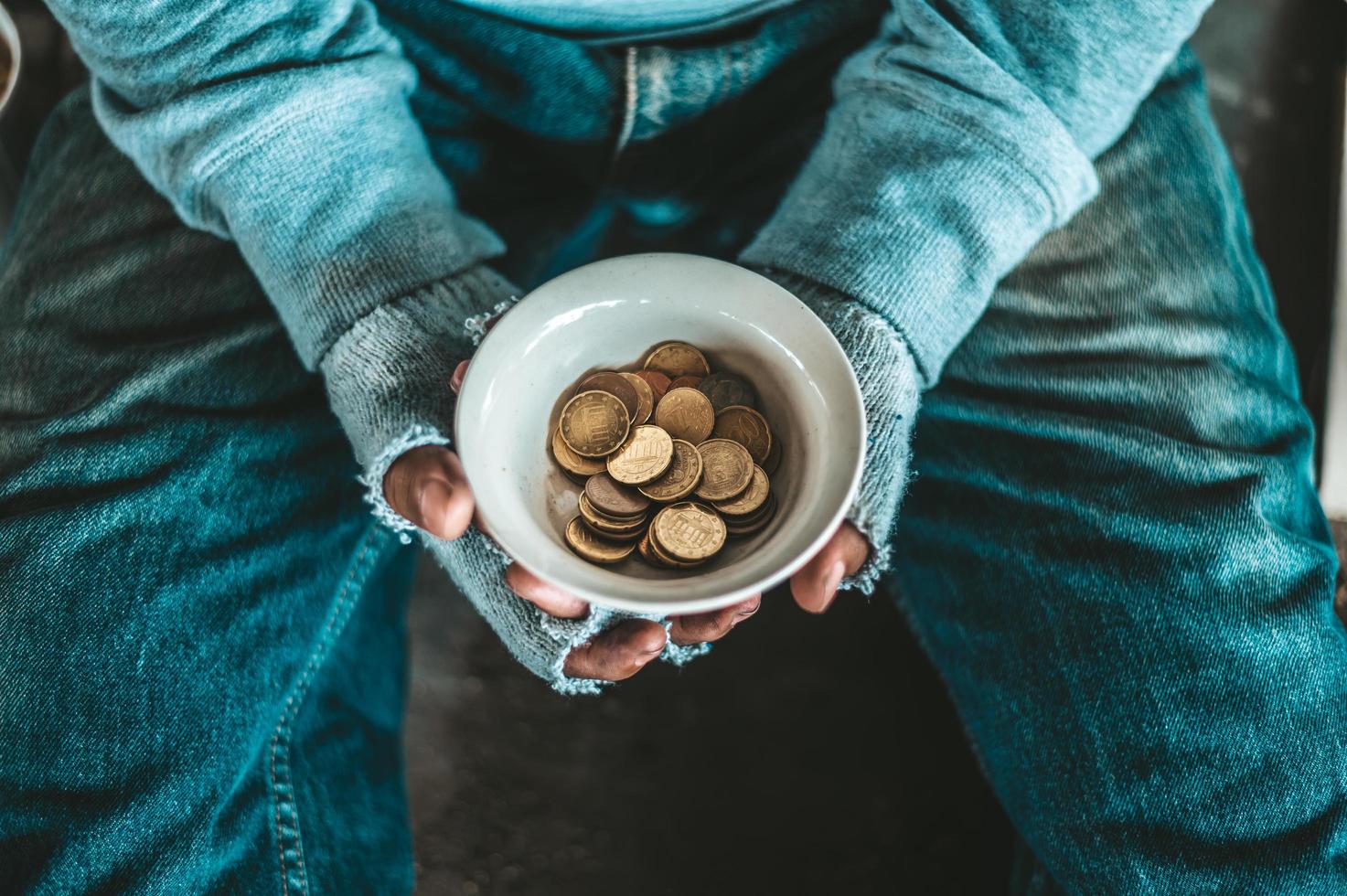 Bettler sitzt unter einer Brücke mit einer Tasse Geld foto