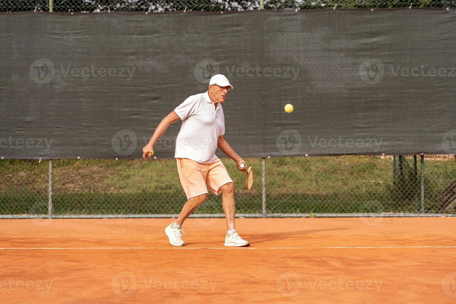 Älterer Tennisspieler in Sportkleidung in Aktion auf einem Sandtennisplatz foto