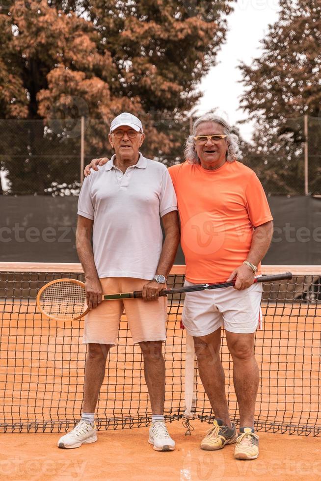 Porträt von zwei älteren Tennisspielern in Sportkleidung, die sich am Ende des Spiels auf einem Sandtennisplatz entspannen foto