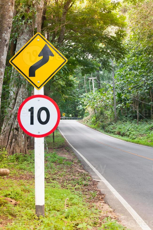 Selektive Geschwindigkeitsbegrenzung Verkehrszeichen 10 und kurvenreiches Straßenwarnsymbol für sicheres Fahren auf der Landstraße im Wald mit Bergblick, zurückhaltend foto