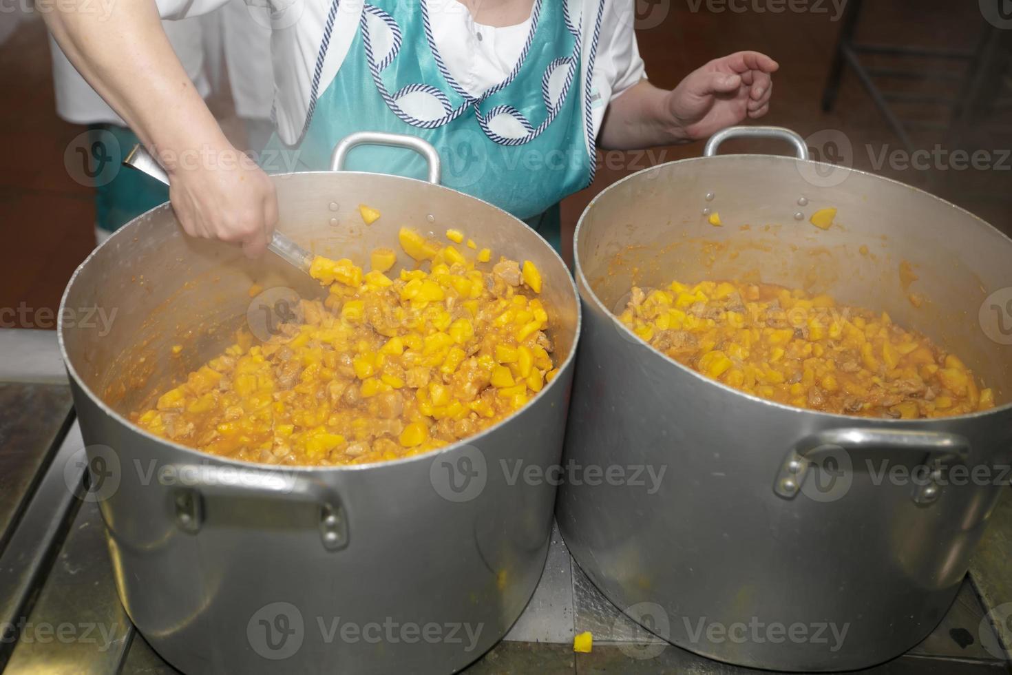 Die Hände eines Kochs rühren Essen in einer großen Metallpfanne in einer Großküche um. foto