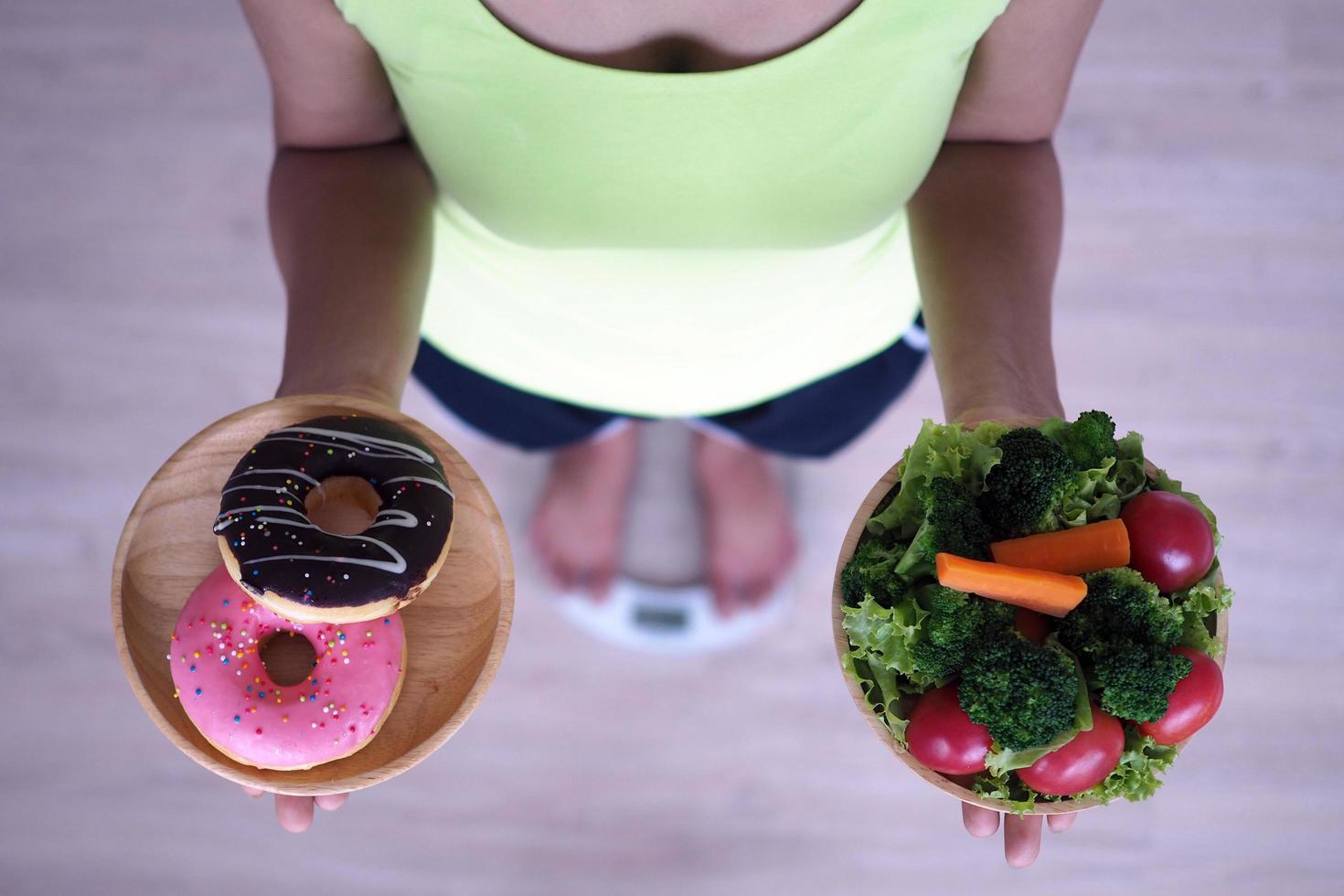 Frauen wiegen mit der Waage, halten Donuts und Salate. Die Entscheidung, Junk Food zu wählen, das nicht gut für die Gesundheit ist, und Gemüse mit hohem Vitamingehalt ist für den Körper von Vorteil. foto