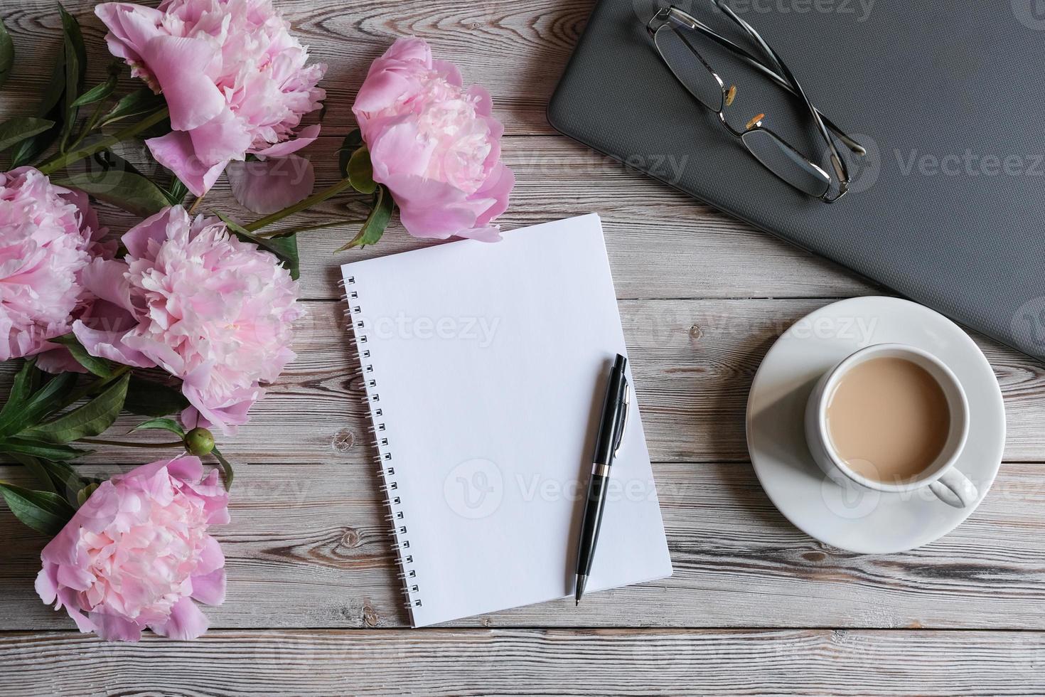 Draufsicht des weiblichen Arbeitsbereichs mit Laptop, leerem Notizblock, Tasse Kaffee und Pfingstrosenblumen. Büro für Frauenarbeit. Mock-up-Notizblock foto