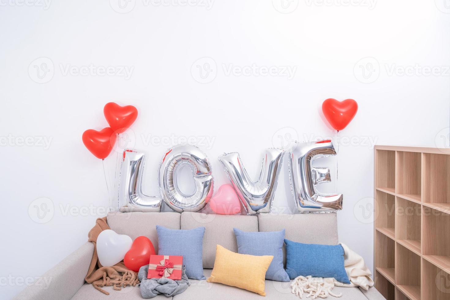 folienliebesballons und geschenke auf einem sofa mit weißer wand im hintergrund zum valentinstag, muttertagsüberraschungsdesignkonzept. foto