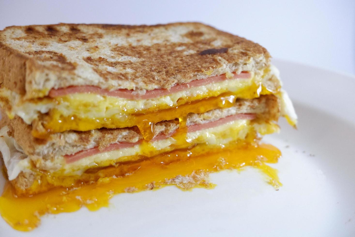 Schinken-Käse-Ei-Sandwich das Eigelb fließt aus dem weißen Hintergrund. Vollkornbrot-Sandwich foto