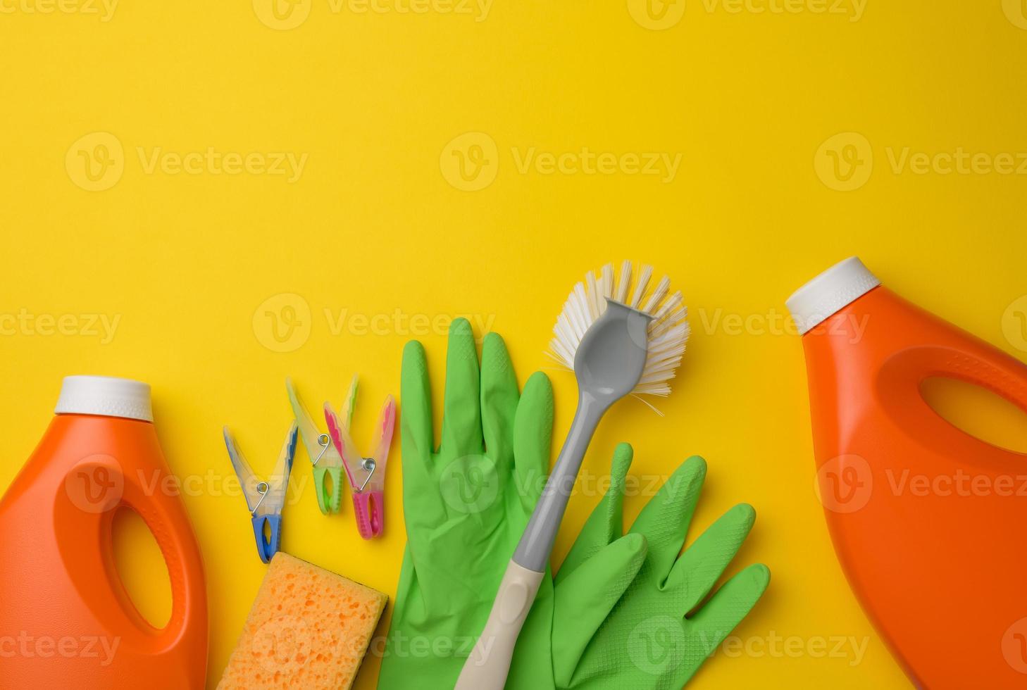 Gummigrüne Handschuhe zum Reinigen, orangefarbene Plastikflasche mit Reinigungsmittel, Bürste auf gelbem Hintergrund, Set foto