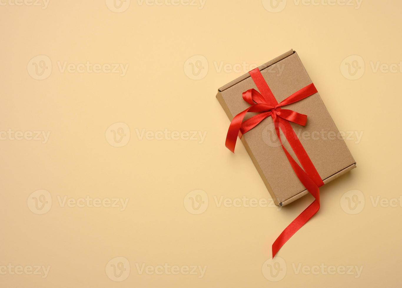 rechteckiger brauner Karton, der mit einem seidenroten Band auf beigem Hintergrund gebunden ist, Ansicht von oben foto