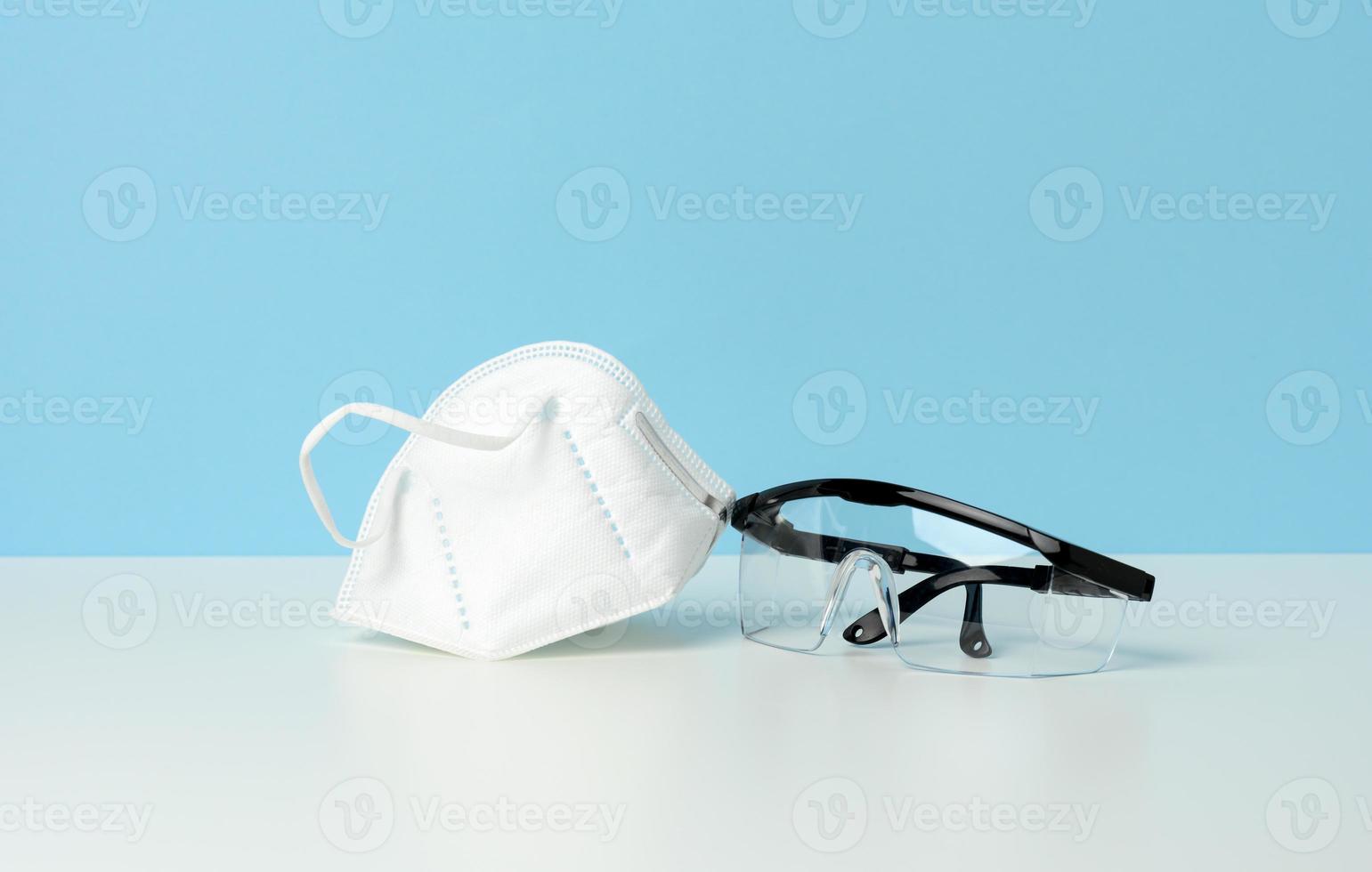 transparente medizinische Schutzbrille aus Kunststoff und weiße Einwegmaske auf blauem Hintergrund foto