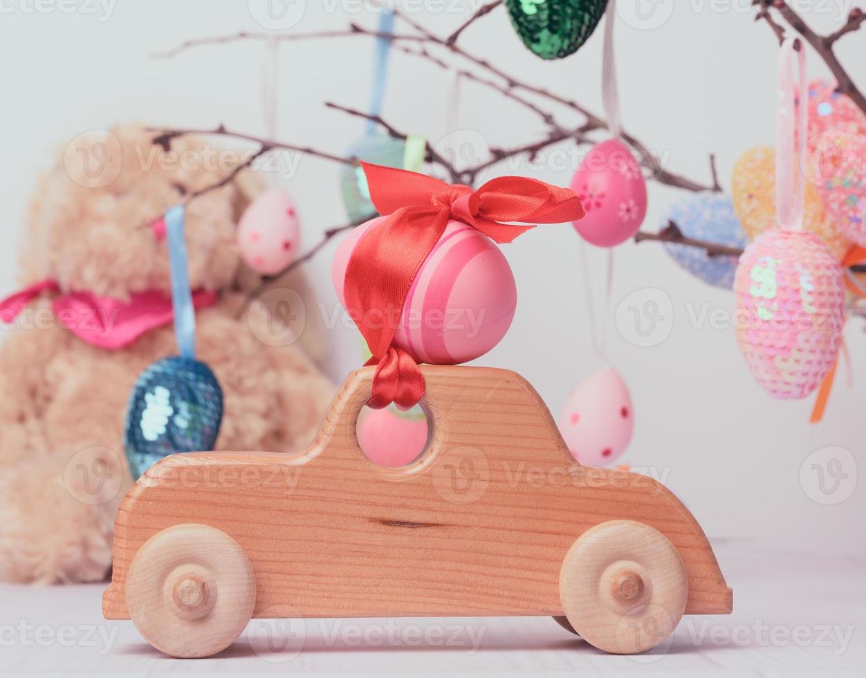 Spielzeugauto aus Holz mit einem rosafarbenen Osterei, das mit einem roten Band befestigt ist foto