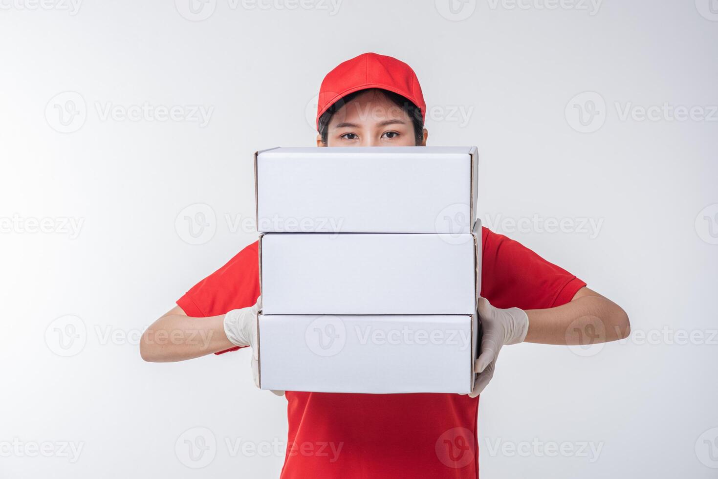 Bild eines jungen Zustellers in roter Kappe, leerem T-Shirt, Uniform, stehend mit leerem weißen Karton, isoliert auf hellgrauem Hintergrund Studio foto