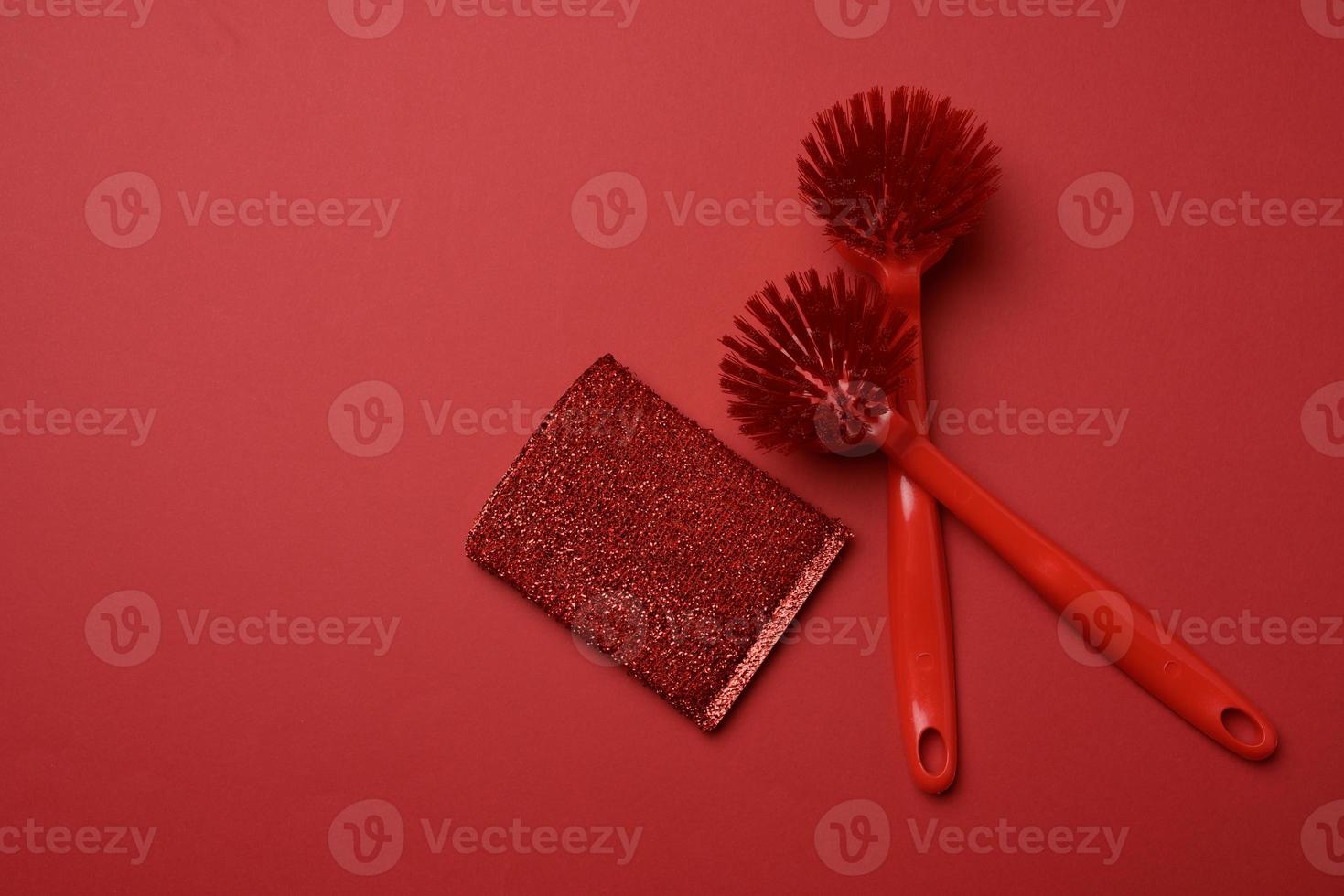 zwei rote kunststoffbürsten und ein schwamm zum spülen von geschirr auf rotem hintergrund foto