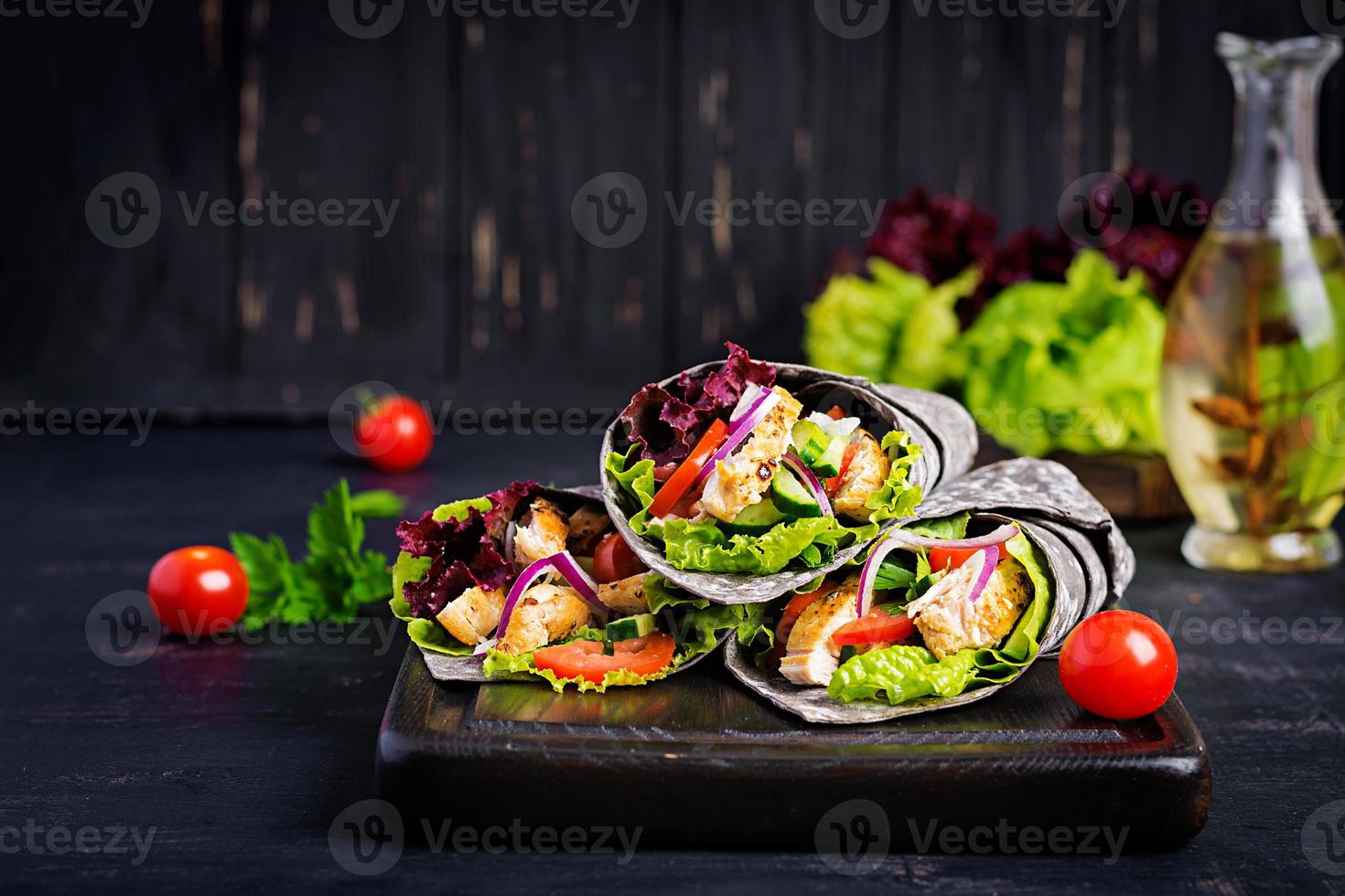 Tortilla mit Tintenfisch-Wraps mit Hähnchen und Gemüse auf schwarzem Hintergrund. Chicken Burrito, mexikanisches Essen. foto