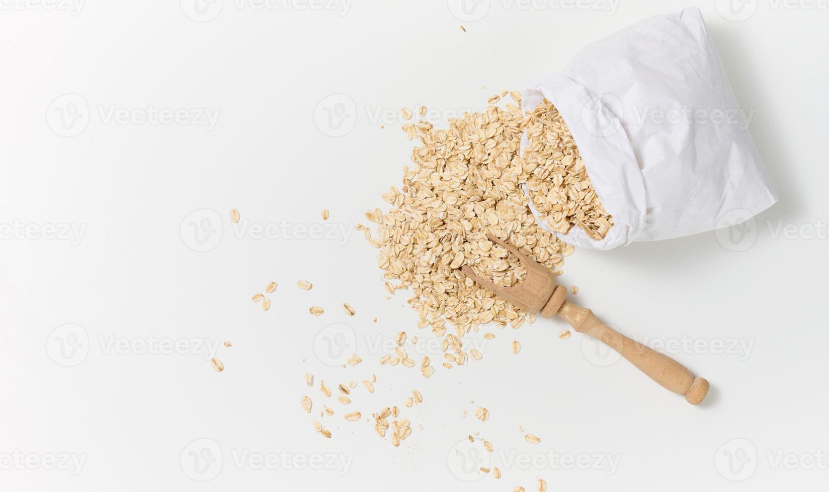 roh Haferflocken im ein Weiß Papier Tasche und ein hölzern Löffel auf ein Weiß Tisch, Frühstück Haferbrei foto