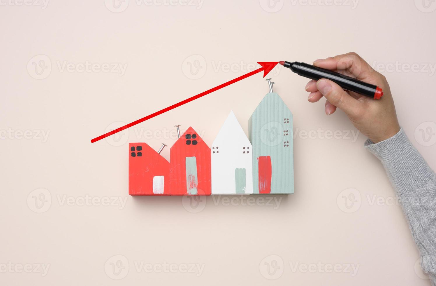 ein Miniatur-Holzhaus und die Hand einer Frau zeichnet ein Diagramm mit wachsenden Indikatoren. foto