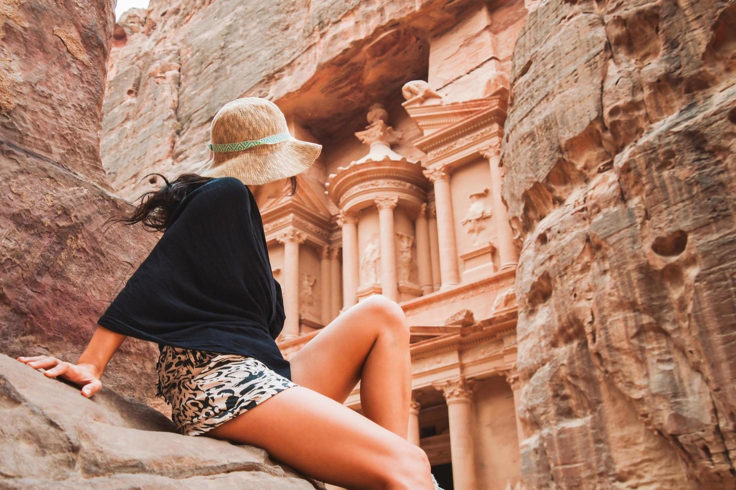 kaukasischer tourist, der auf einem aussichtspunkt in der antiken stadt petra sitzt und die schatzkammer oder al-khazneh, das berühmte reiseziel von jordanien, betrachtet. Unesco-Weltkulturerbe foto