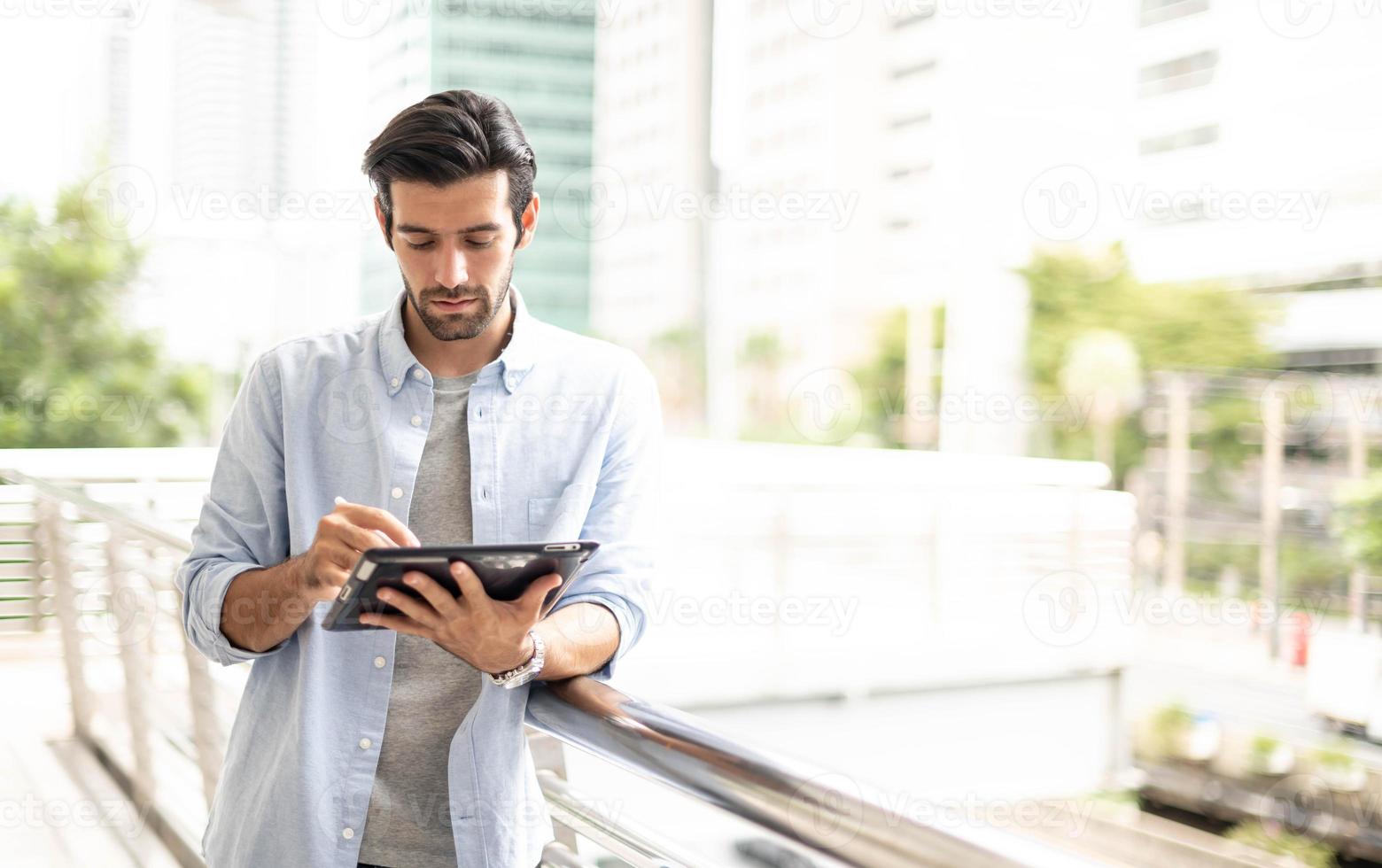der junge mann, der ein tablet benutzt, um außerhalb des büros zu arbeiten. der mann, der lässige kleidung trägt und sich nachdenklich und ernst fühlt. foto