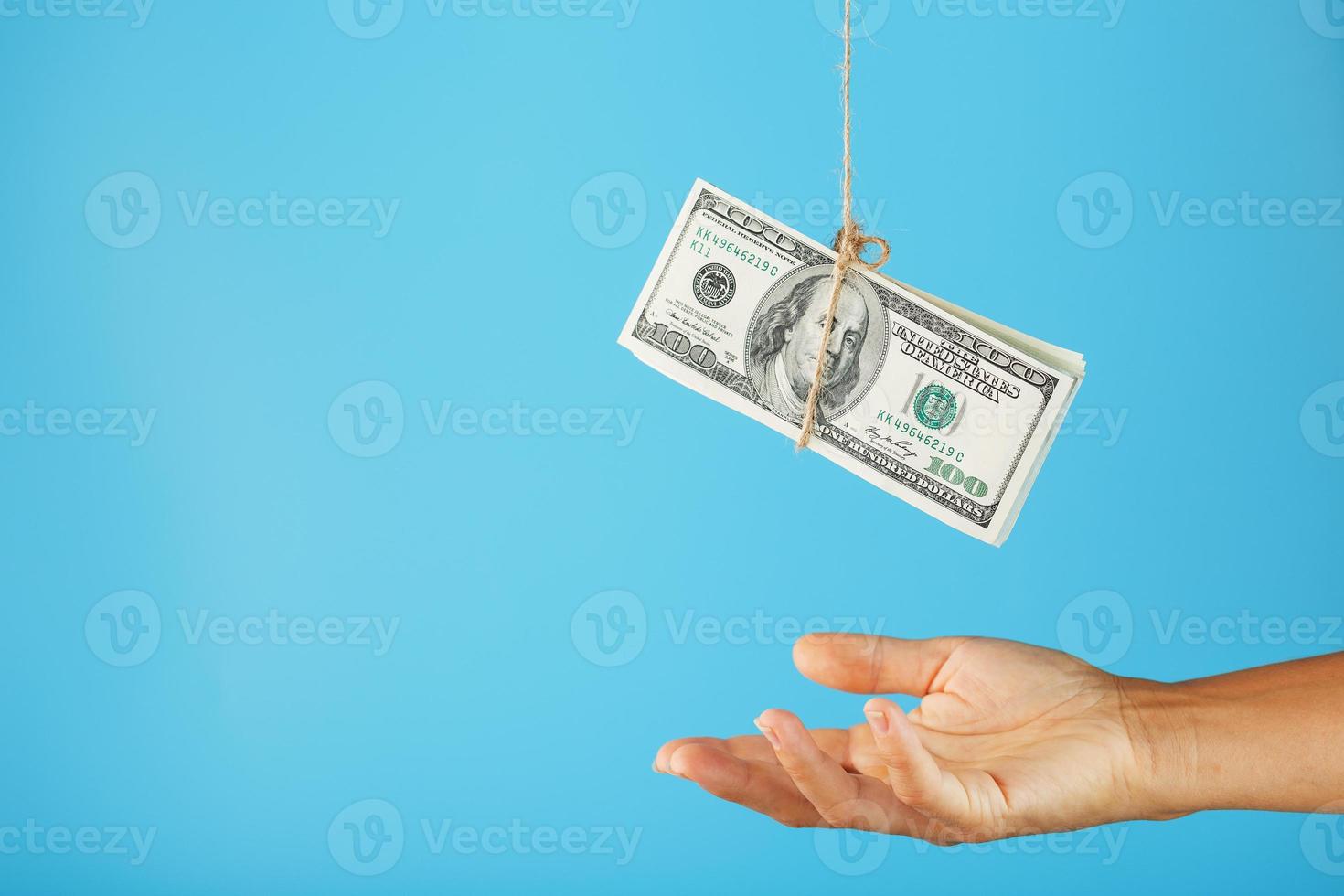 Ein Bündel Dollar an einer Schnur über einer menschlichen Handfläche auf blauem Hintergrund. foto