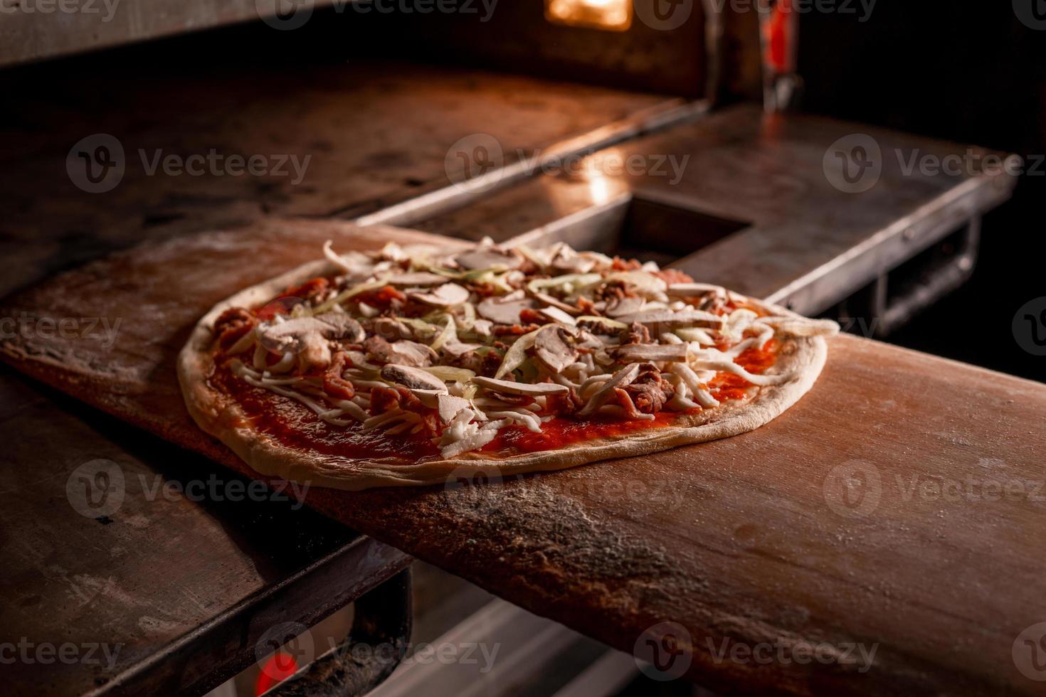 Pizza backen im Pizzarestaurant. Holzbefeuerter traditioneller Pizzaofen. Pizza in der Küche machen. Klassisches Steinofen-Brennholz herstellen foto