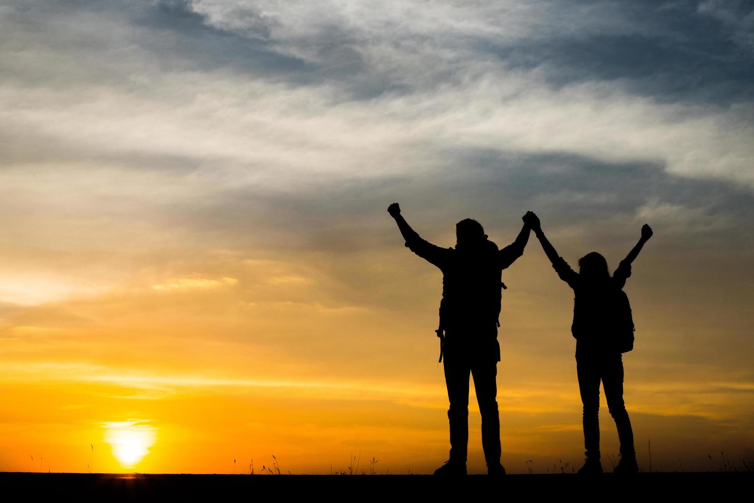 Silhouetten von zwei Wanderern mit Rucksäcken, die den Sonnenuntergang genießen foto