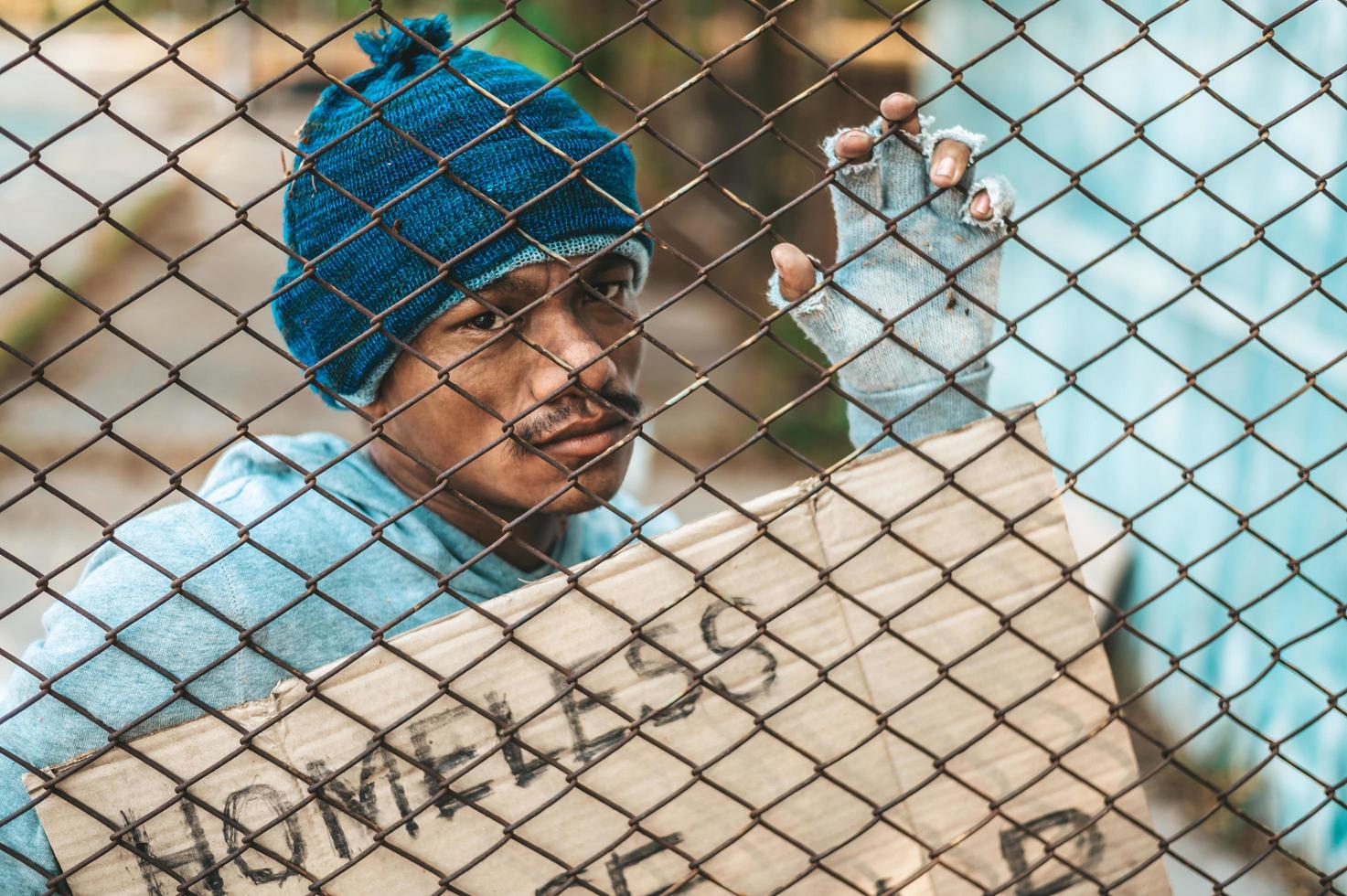 Bettler an einem Zaun mit obdachlosen Nachrichten bitte helfen foto