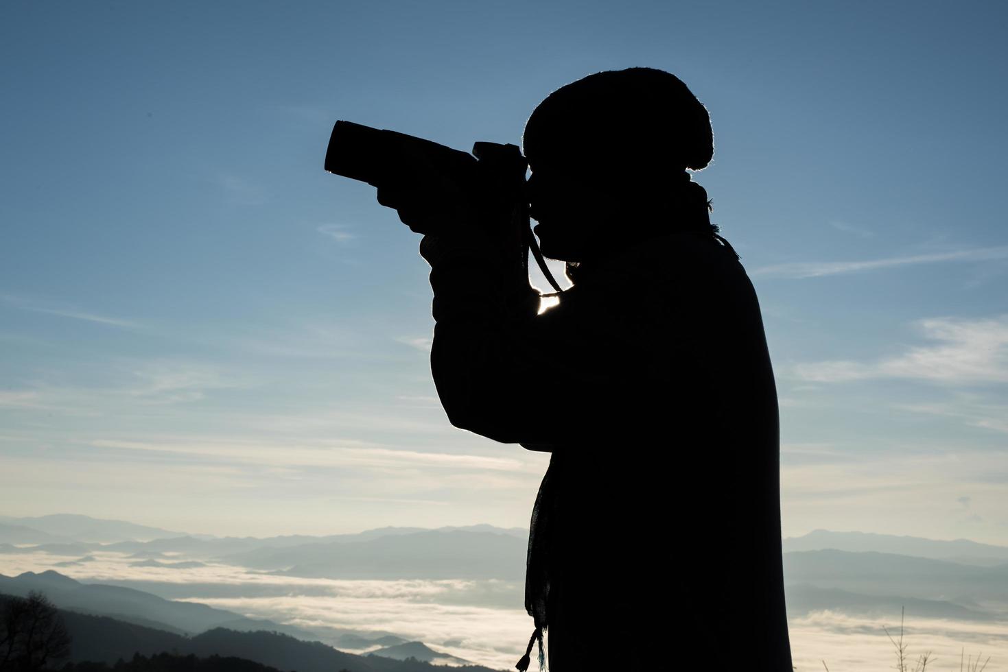 Schattenbild des jungen Fotografen, der eine Kamera mit Berglandschaft hält foto