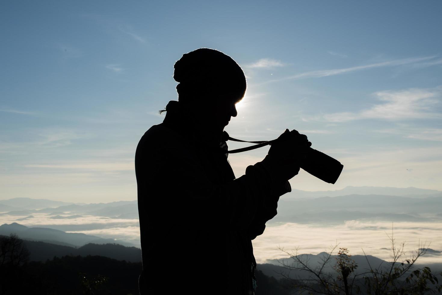 Schattenbild des jungen Fotografen, der eine Kamera mit Berglandschaft hält foto
