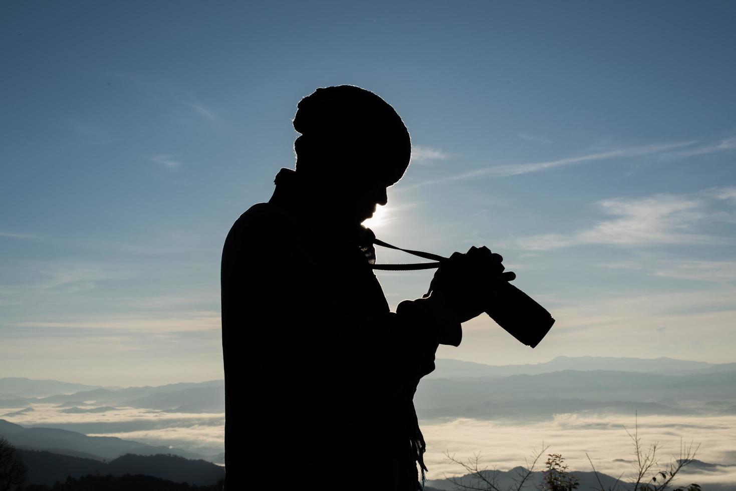 Schattenbild des jungen Fotografen, der eine Kamera mit Berglandschaft hält foto