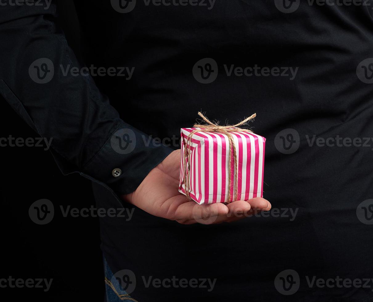 männlich Hand hält ein papierverpackt Box mit ein Geschenk hinter seine zurück foto
