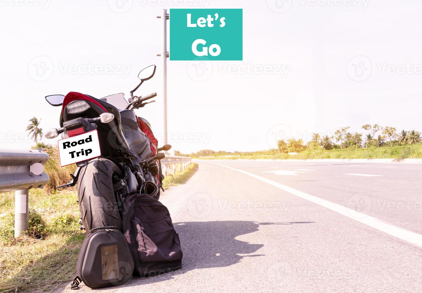 Motorrad geparkt und schwarz Rucksack mit Botschaft Lasst uns gehen auf Grün Straßenschild auf Autobahn Straße Aussicht foto