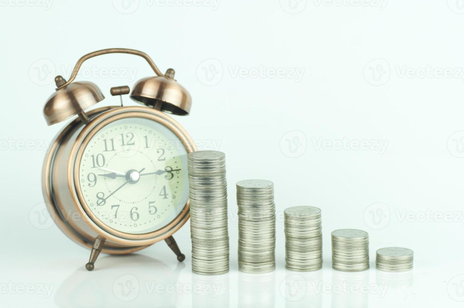 Wecker und Stapel von Münzen auf weißem Hintergrund foto