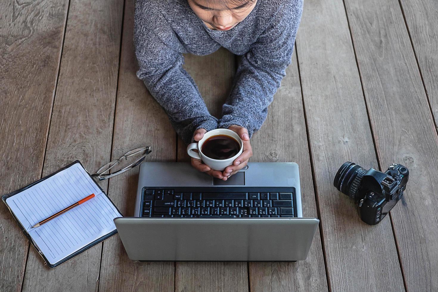 Frau, die auf dem Boden liegt und an einem Laptop arbeitet foto