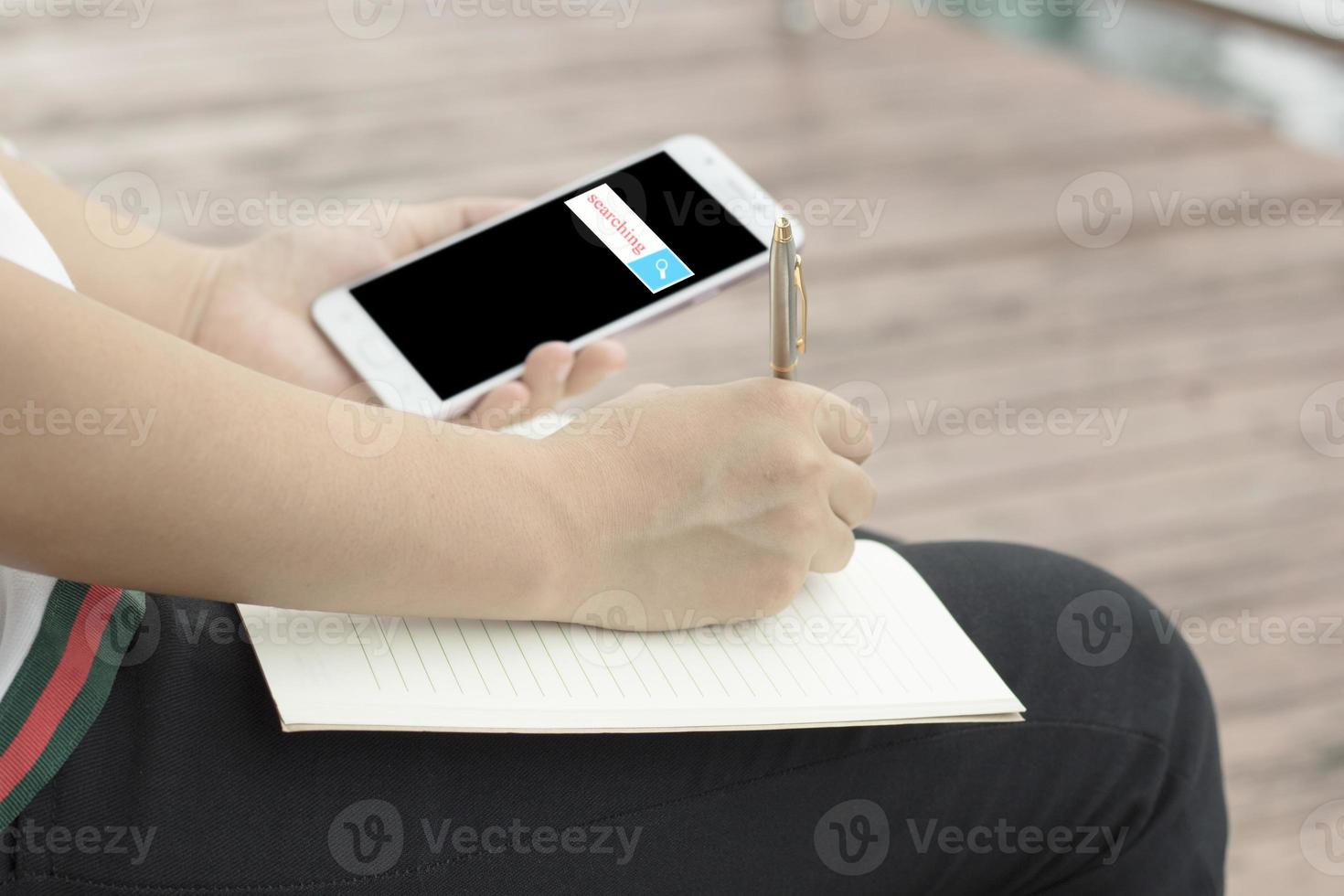 Person, die auf einen Notizblock schreibt, während sie Telefon betrachtet foto