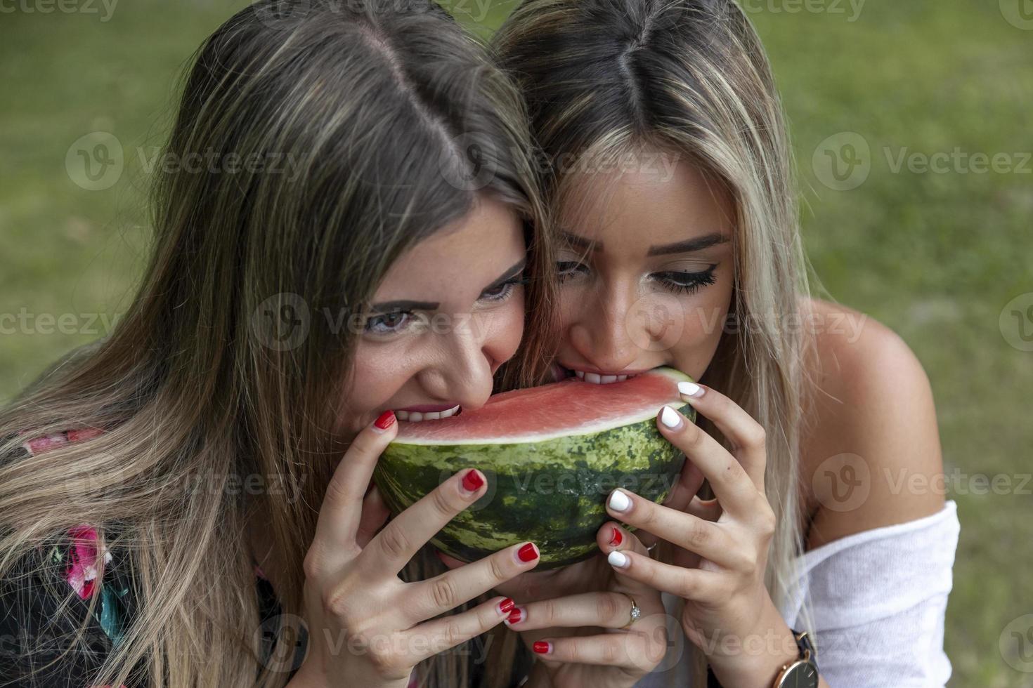 Paar von jung schön Frauen Essen ein Scheibe von frisch Wassermelone foto