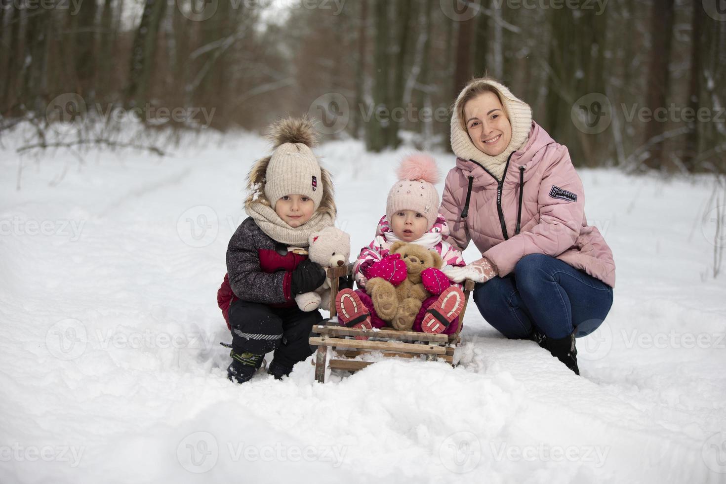 Mama und Kinder auf ein Jahrgang hölzern Schlitten gegen das Hintergrund von ein Winter Wald. Frau mit Kinder auf ein Winter gehen. foto