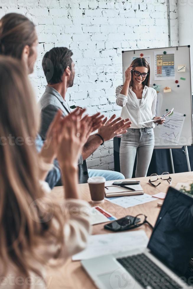 Teilen interessant Ideen. Gruppe von Geschäft Menschen klatschen und lächelnd während Stehen im das Tafel Zimmer foto