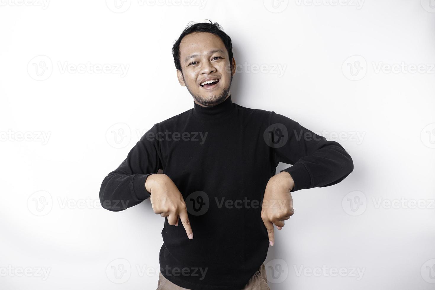 aufgeregt asiatisch Mann tragen schwarz Hemd zeigen beim das Kopieren Raum unten ihn, isoliert durch Weiß Hintergrund foto