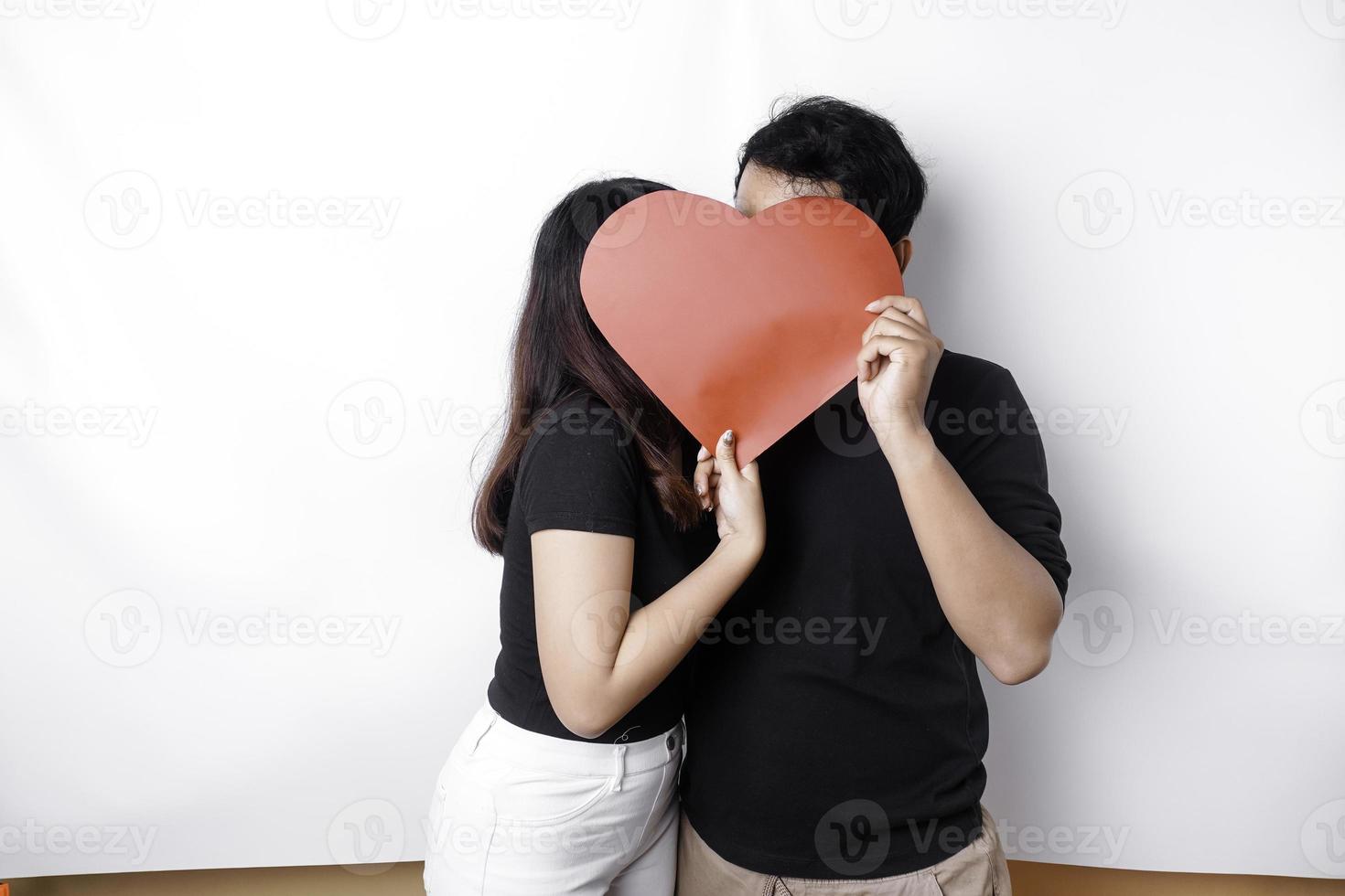 ein Paar im Liebe hält ein Papier rot Herz, Abdeckung ihr Gesichter. glücklich Valentinstag Tag foto